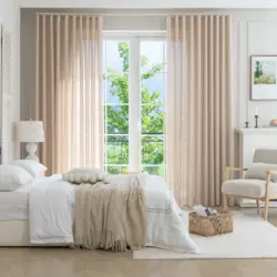 Twee panelen beige Olivia vitrage van plafond tot vloer naast een openslaande deur in een lichte slaapkamer