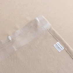Achterkant van beige Olivia vitrage met transparante plooiband, witte haakjes, zijzoom en merklabel met wasvoorschriften