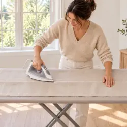 Vrouw vouwt het gordijn om op de nieuwe lengte en strijkt de vouw plat op een strijkplank